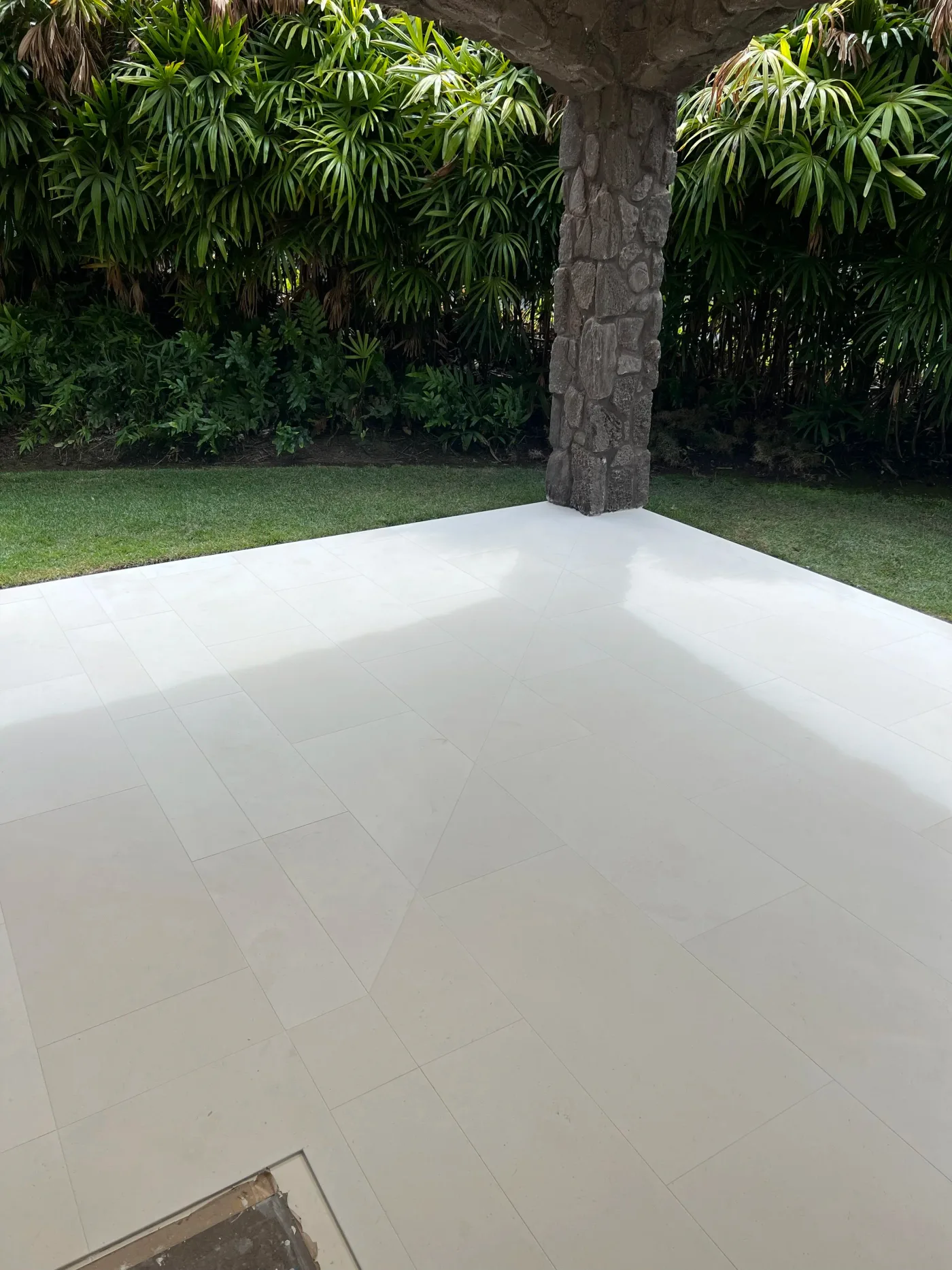 Covered lanai floored in large-format limestone tile beside a lava-rock column and tropical plants
