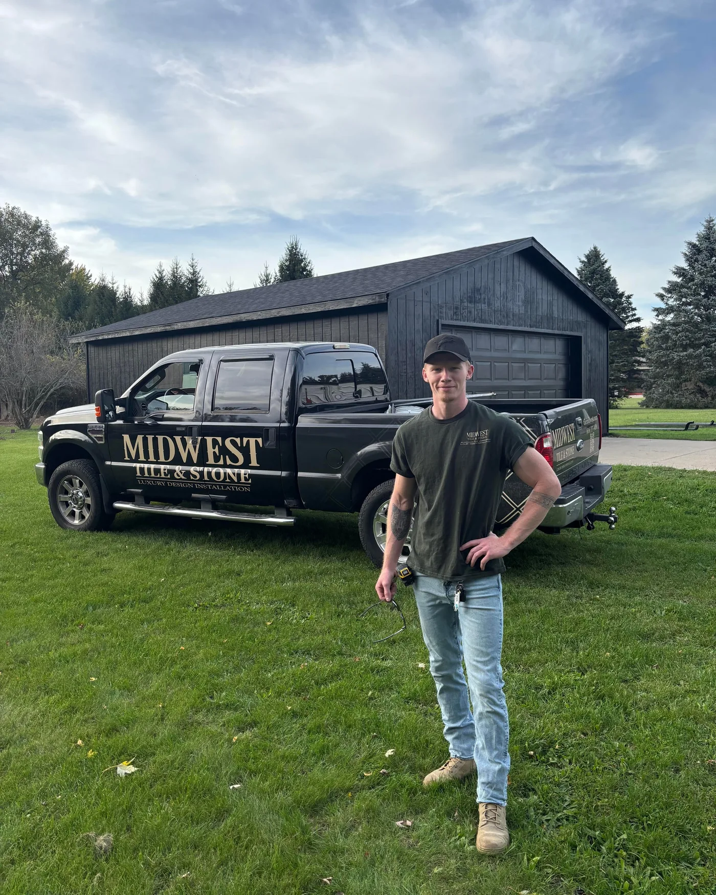 Austin Portmann, owner of Midwest Tile & Stone, standing in front of his black work truck lettered with the company logo