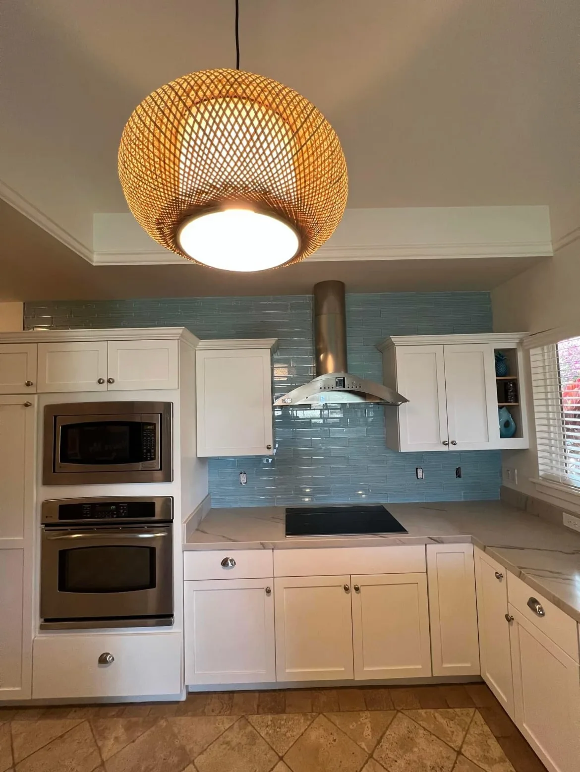 Kitchen backsplash in blue glass linear tile running up to the ceiling behind a stainless chimney hood, with white shaker cabinets