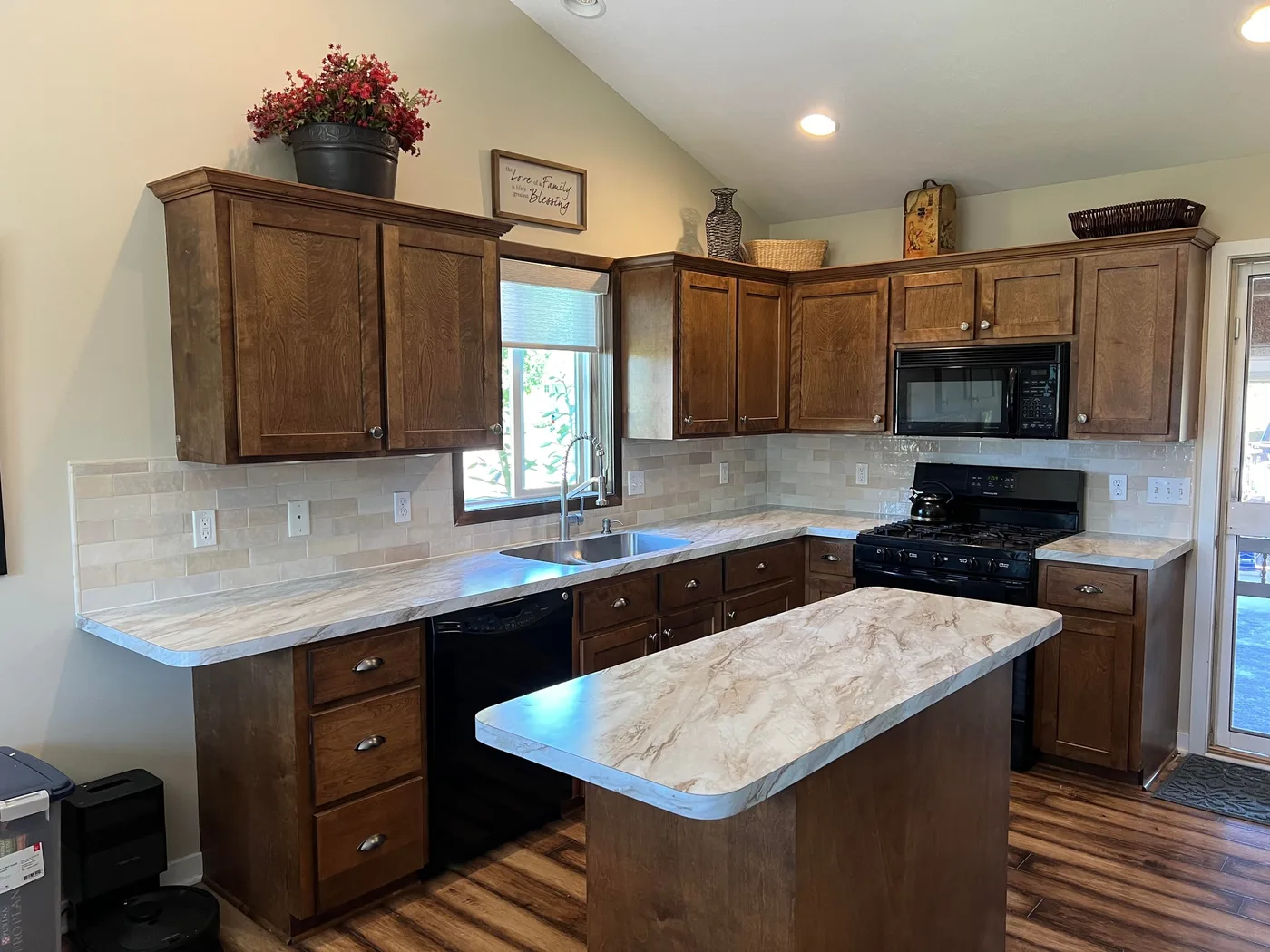 Kitchen with stained wood cabinets and a cream handmade-look subway tile backsplash around a window and gas range