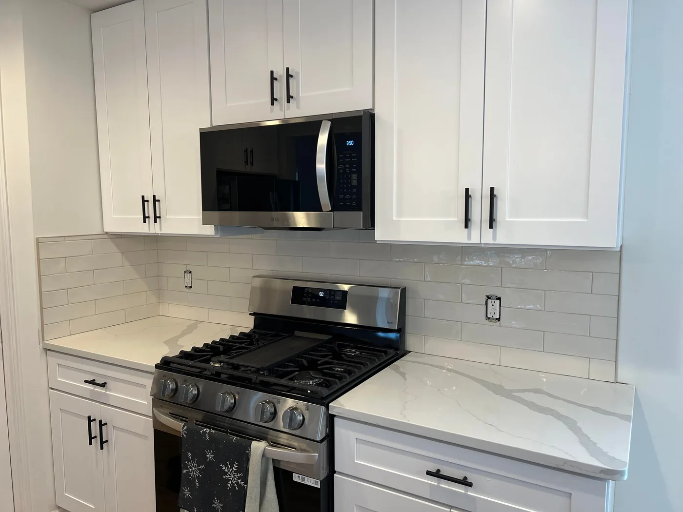 Range wall with a long white handmade-look subway tile backsplash between white shaker cabinets and a stainless microwave