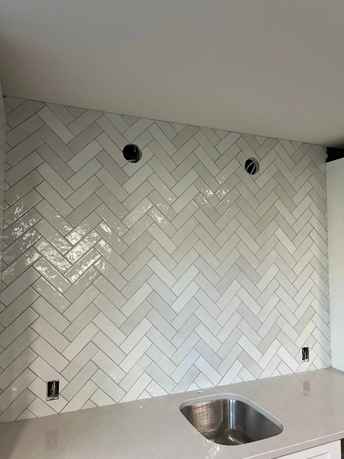 Wall-to-ceiling kitchen backsplash in glossy white handmade-look tile laid in a herringbone pattern above a quartz counter and undermount sink