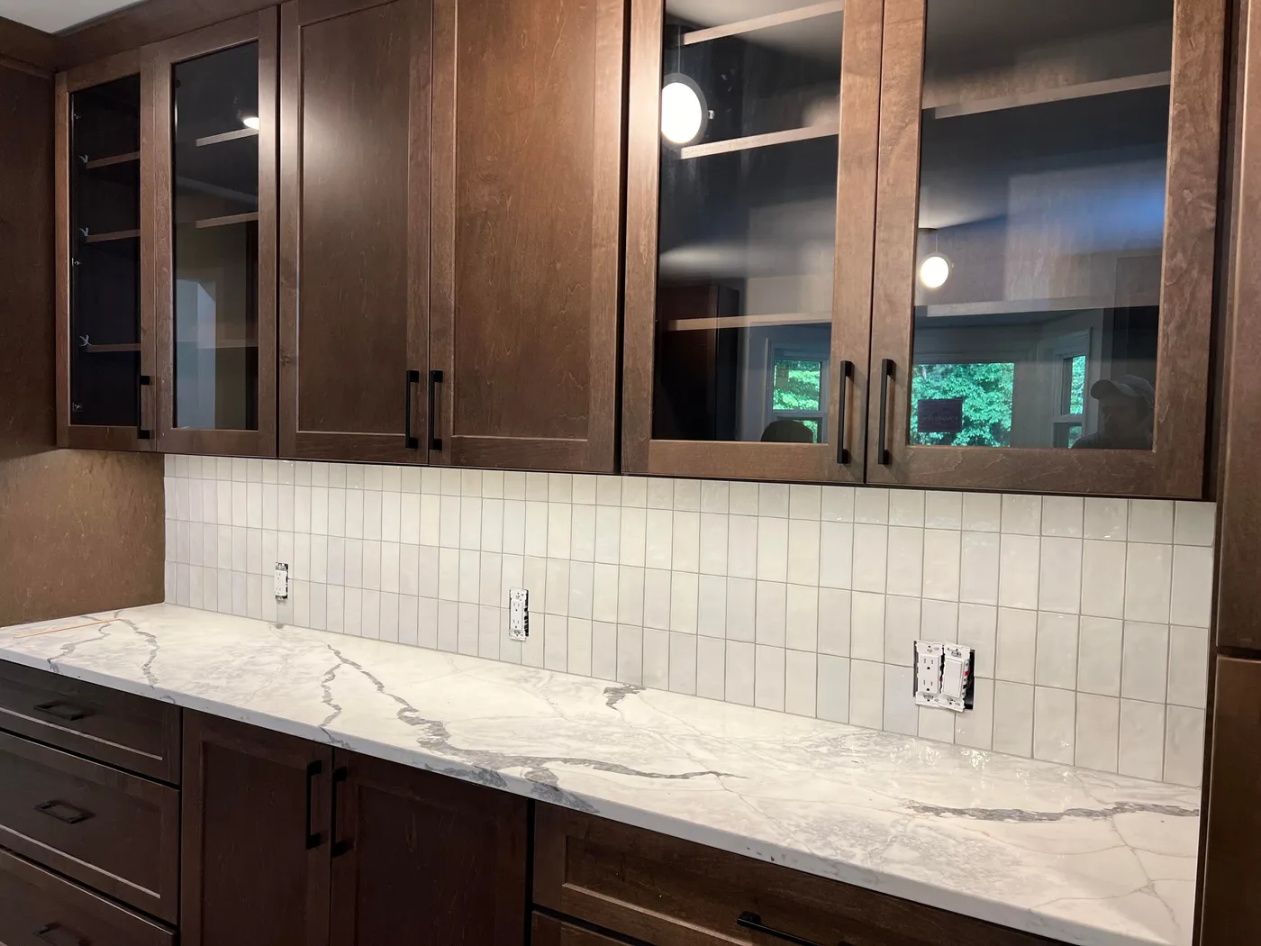Backsplash of white handmade-look tile in a vertical stack under glass-front wood cabinets, above a white quartz counter