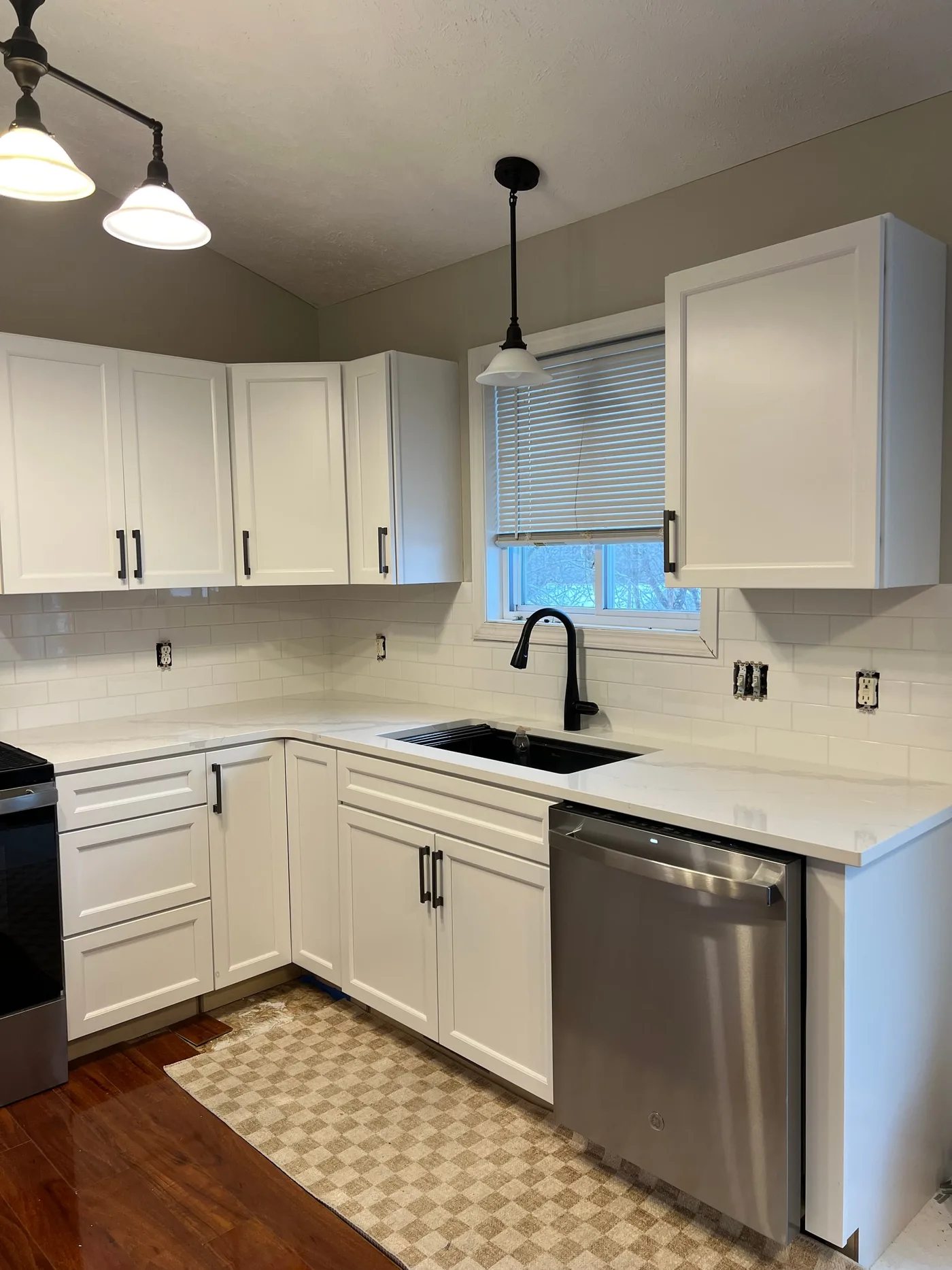 White kitchen with a classic white subway tile backsplash around a window and black faucet, with quartz counters and white shaker cabinets